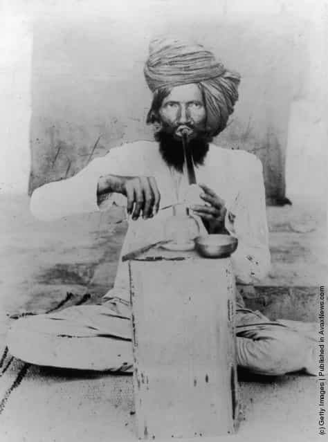 circa 1900: A man in a turban sits cross-legged smoking opium in Meywar, Rajputana
