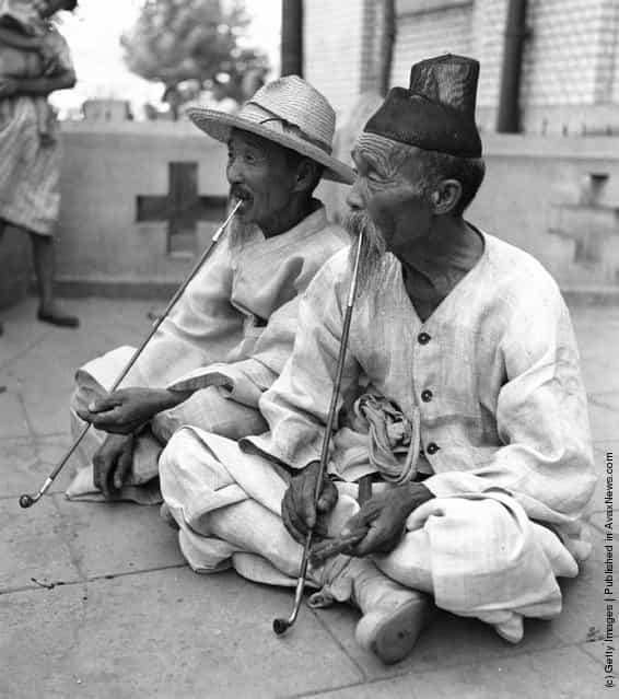 August 1950: Two elderly men smoking pipes of opium on a terrace in Korea