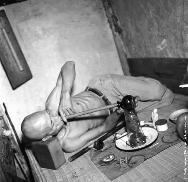 circa 1955: A narcotic addict in the British Crown Colony of Hong Kong smokes from a home-made hookah pipe made of an earthen jug and a bamboo stick