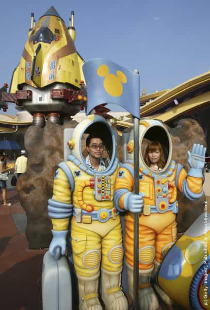 Tourists pose for pictures with decorations featuring space suits at the Tomorrow World in the Hong Kong Disneyland