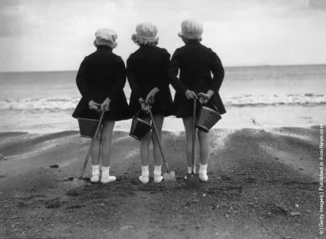 Wearing coats and berets against the chill of an English summer three children have brought their buckets and spades to the beach at Whitby in Yorkshire, 1930