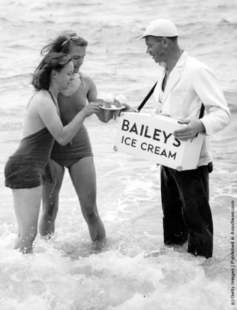 An ice cream vendor wearing waders sells Bailey's ice cream to two women bathing in the sea at Brighton, 1939