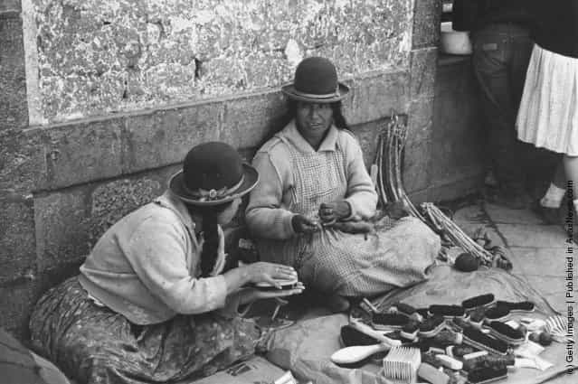 Two Peruvian Indian women, wearing traditional bowler-style hats, sell home-made brushes in a street market, 1955
