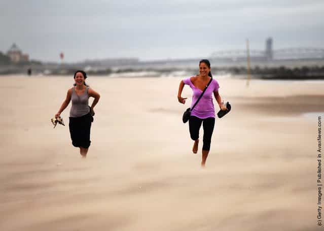 Women run along a sand-swept beach at Coney Island following heavy rain and winds from Hurricane Irene