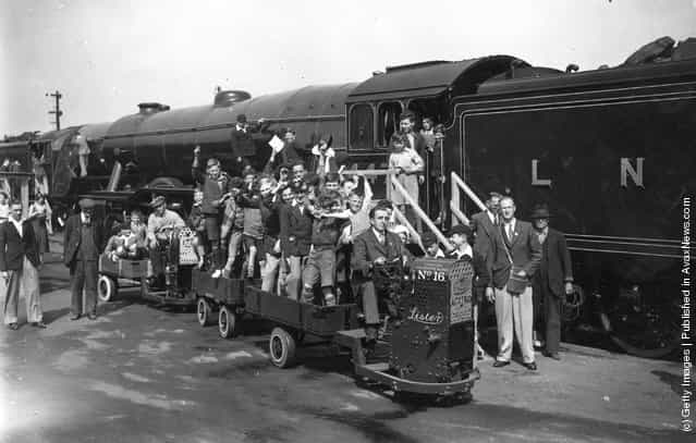 A miniature truck carrying a party of children in open carriages next to a London and North Eastern railway steam engine on a platform at Ilford railway station