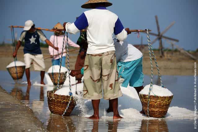 A farmer carries baskets of salt during a harvest in the the salt production process in Sumenep on Madura island, Indonesia