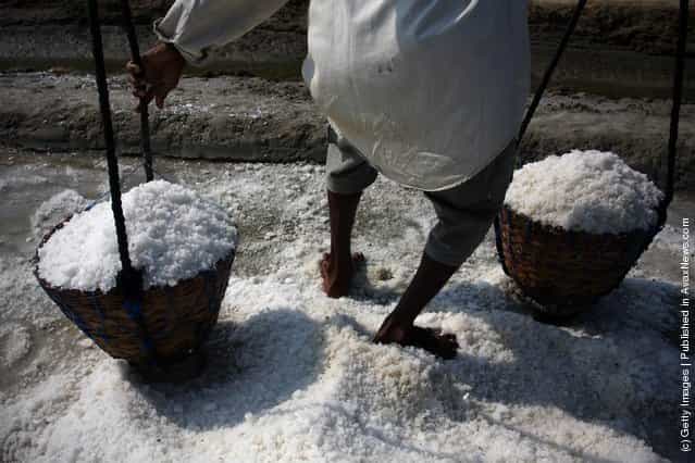 A farmer carries baskets of salt during a harvest in the the salt production process in Sumenep on Madura island, Indonesia