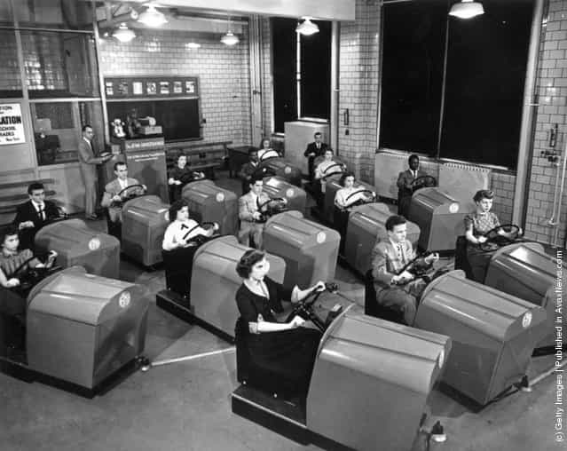 1953: Students at Brooklyn High School in New York learn to handle the controls of a car and experience simulated traffic conditions flashed onto a screen by means of projected film, using the Aetna Drivotrainer