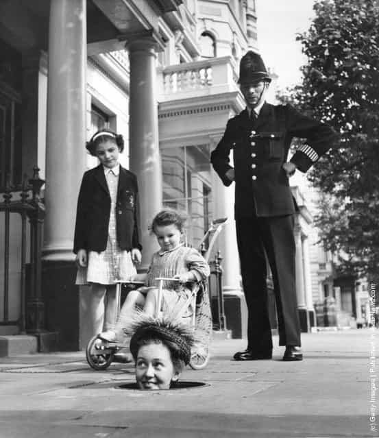 Former child actress Janette Scott emerges from a coal hole wearing one of Kensington-based designer Geynne Mallard's hats, to the interest of a policeman and two girls