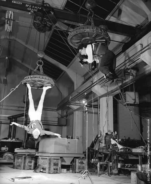 Fox Photos photographer Derek Berwin is hoisted up on an electromagnet at the Boxmag works in Birmingham, in order to take a photograph of typist Kathleen Reddington who is similarly suspended, December 1957
