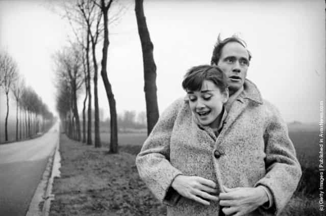 American actor Mel Ferrer buttons up his coat around his wife, actress Audrey Hepburn, on a country road outside Paris, 1956