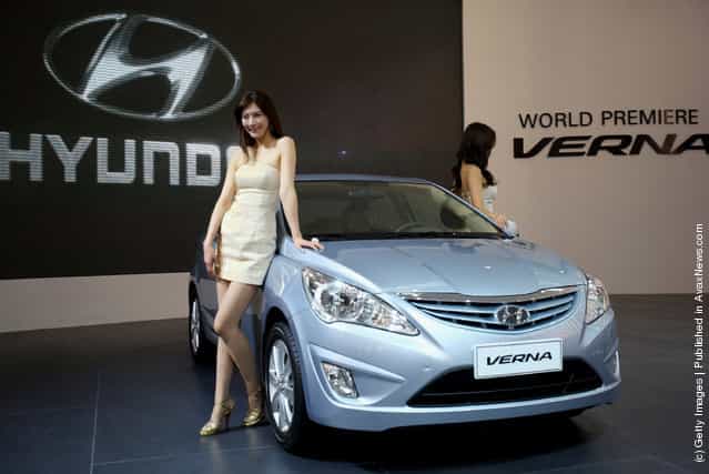 Two models stand beside the world premiere display of Hyundai VERNA car