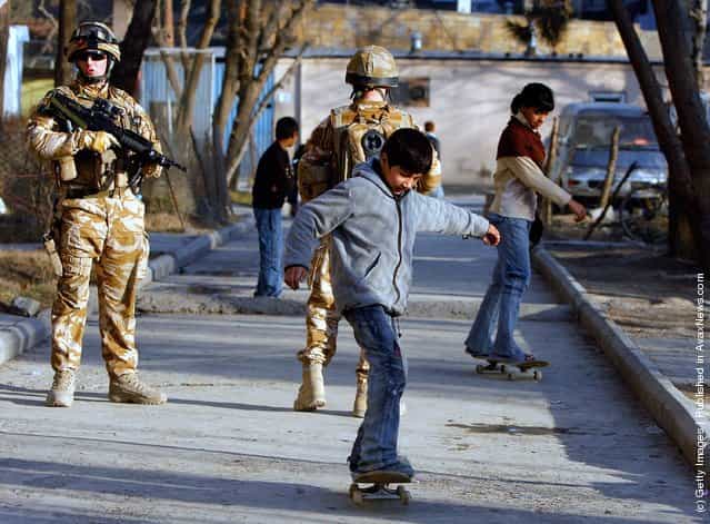 Afghan kids skateboard near their homes along side British ISAF soldiers on patrol