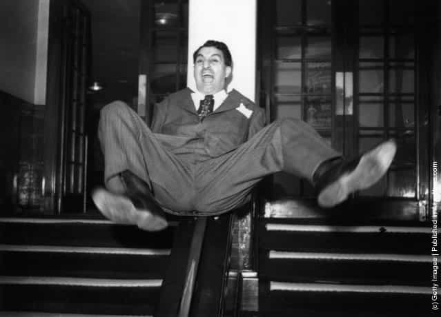 1950: American comedian and actor Danny Thomas sliding down the bannisters at a reception given in his honour