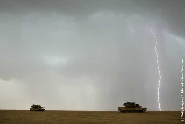 A lighting bolt flashes in the sky as U.S. Army M1A1 Abram tanks roll through the desert