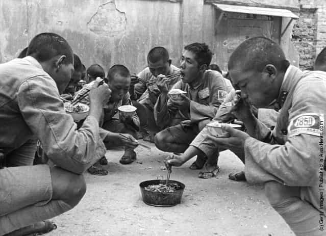 1939: A group of Chinese soldiers squatting and eating from bowls with chopsticks