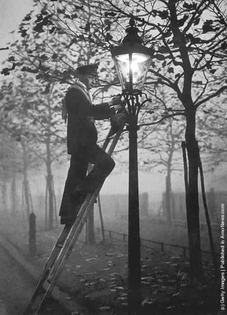A lamp lighter relighting a gas lamp in the fog on November 17, 1930