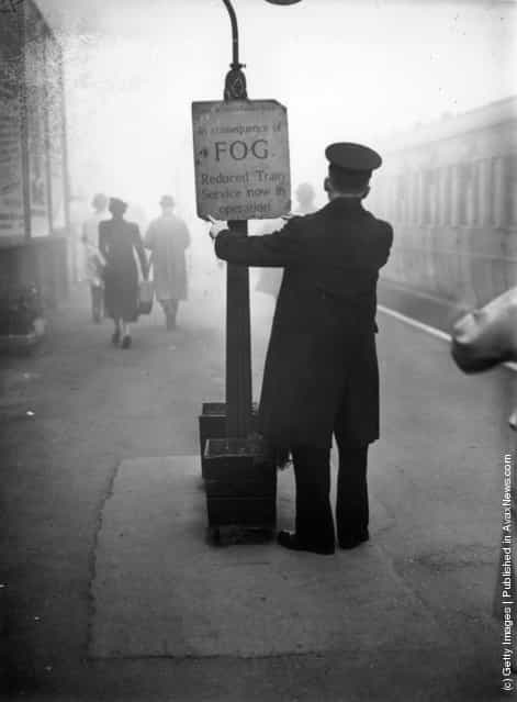 1938: A rail worker fixing a fog warning notice at South Woodford Railway Station in Essex