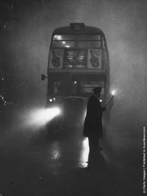 A man guiding a London bus through thick fog with a flaming torch, 1952