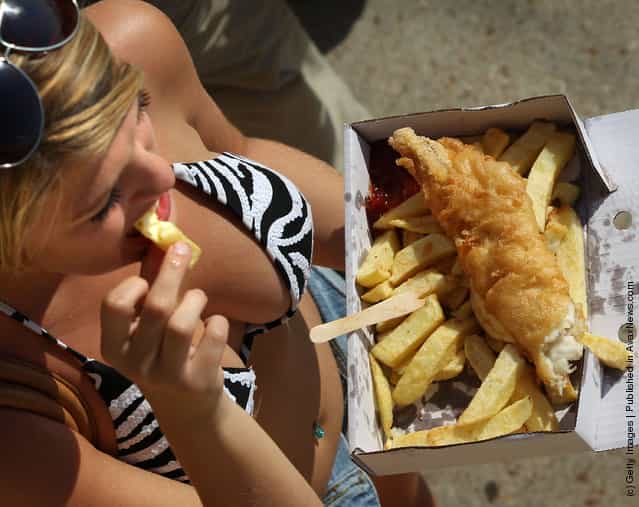 A sexy woman eats fish and chips on the beach