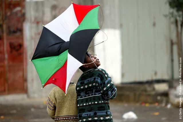 A Palestinian boy looks back as the wind turns his umbrella, made up of the Palestinian national flag colors