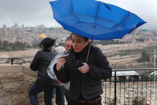 The wind turns a tourists umbrella out as she braves a winter storm to enjoy the view of the Old City from the Mount of Olives