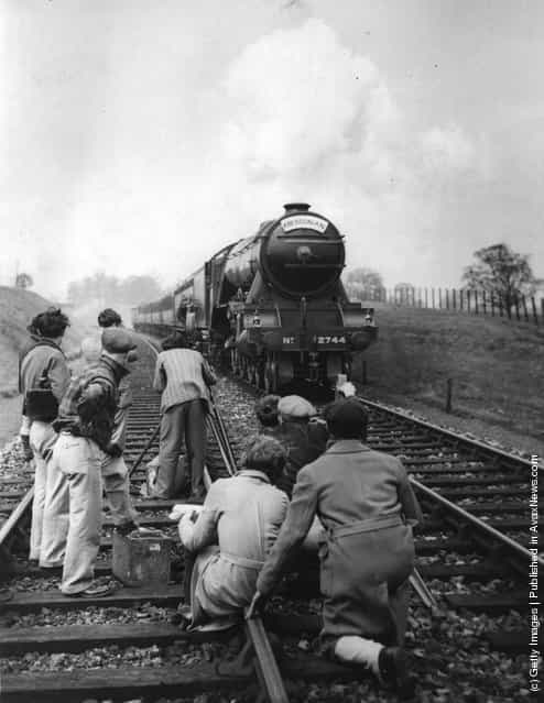 1934: Cameramen on the railway track getting a shot of the Aberdonian express train, with an actor disembarking on to a tender, for the film Night Mail, directed by Herbert Smith