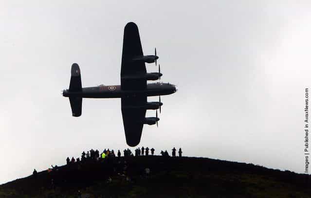 Spectators on a hill look on as a Lancaster bomber flies over Ladybower reservoir in the Derbyshire Peak District to mark the 65th anniversary of the World War II Dambusters mission