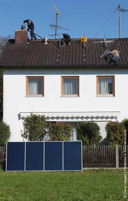Workers install solar power modules for producing heat on the roof of a house