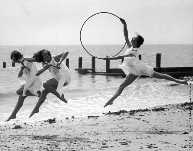 1935: Three members of a dance school rehearse for an upcoming performance on the beach at Worthing. One dancer with a hoop pursues two others with small pipes