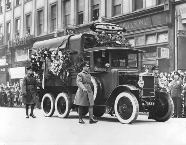 1930: An RAF lorries decorated with flowers including a model of the R101 airship, in a funeral procession for victims of the R 101 airship crash, watched by large crowds