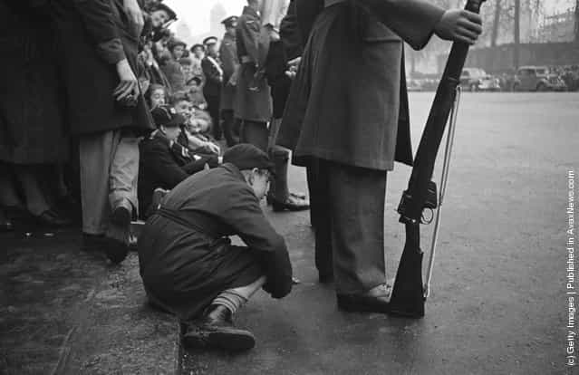 A boy peers under the legs of an RAF serviceman for a glimpse of the wedding procession of Princess Elizabeth (later Queen Elizabeth II) and Philip Mountbatten, Duke of Edinburgh, London, 20th November 1947