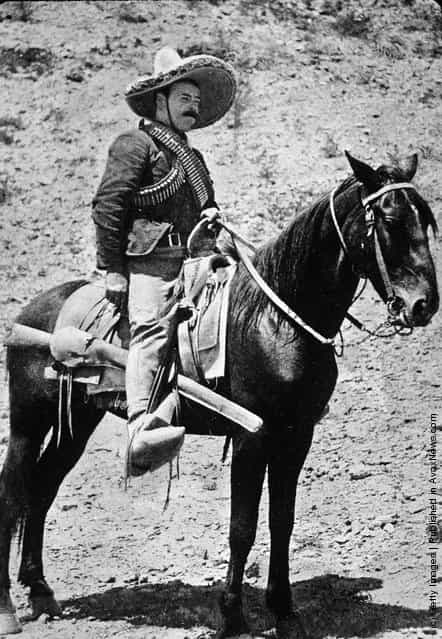 Mexican revolutionary Pancho Villa sits on horseback, wearing a straw hat and ammunition strapped across his shoulders, 1910s