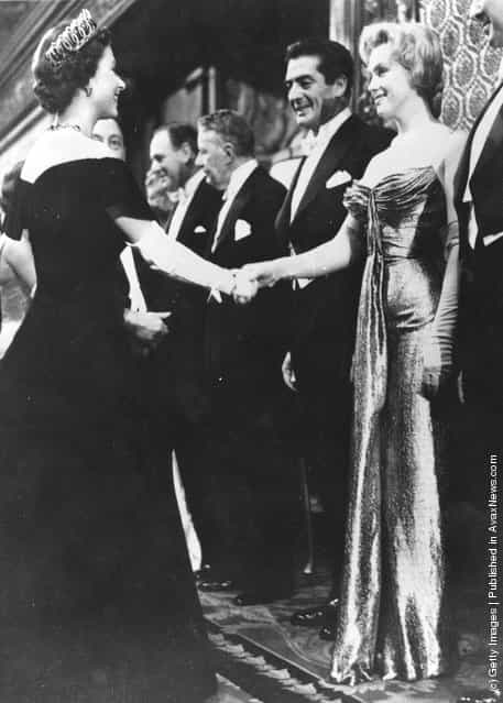  Queen Elizabeth II shaking hands with Marilyn Monroe (1926 - 1962) who stands next to Victor Mature (1913 - 1999) at a Royal Film Performance of The Battle of the River Plate at the Empire Theatre, Leicester Square, London