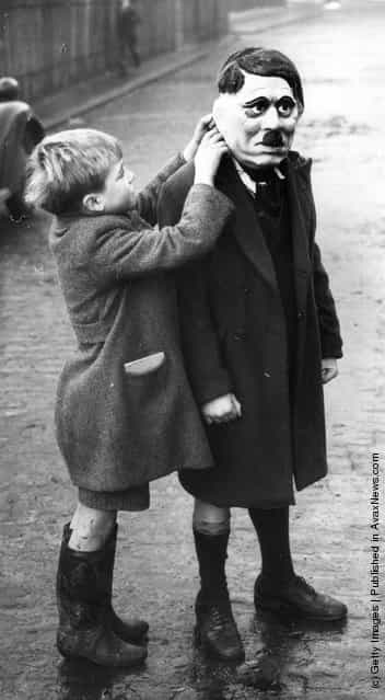 A young boy adjusts his friends Adolf Hitler mask during a game on a street in Kings Cross, London, 1938