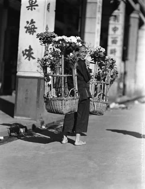 1920s: Female paper flower vendor carrying two large baskets of artificial flowers, Hong Kong