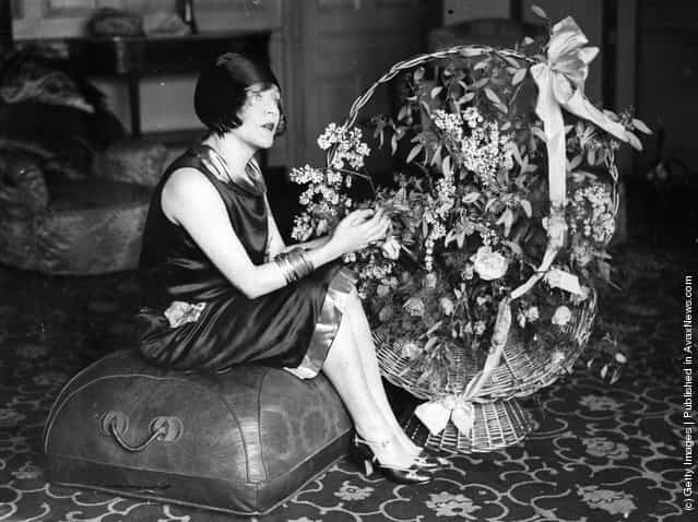 1925: American film star, Mae Murray (1889 - 1965) seated on a pouffe with a large basket of flowers