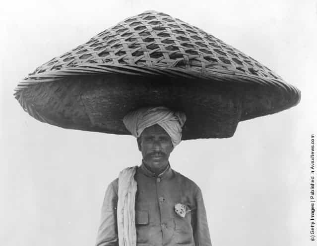 1934: A Singhalese man carrying a pile of clothing in a large closed basket on his head that looks like an enormous mushroom shaped hat