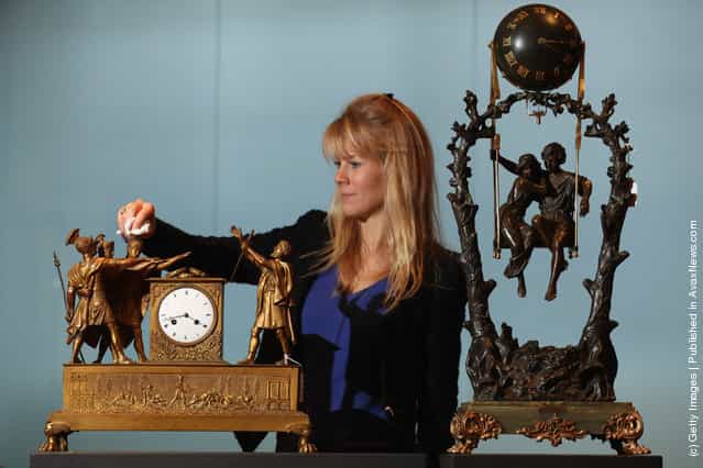 A gallery assistant cleans an ormolu mantel clock next to spelter and onyx mystery swinging clock in Bonhams auction house