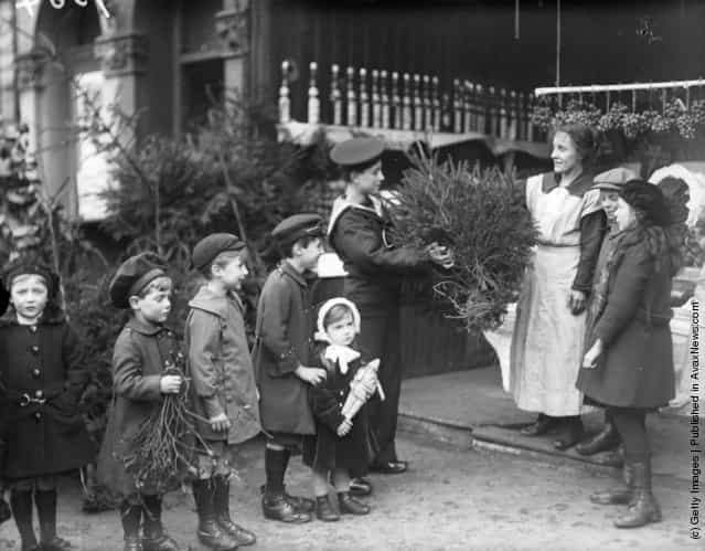 1918: A young sailor buys a Christmas tree at a greengrocers and a young boy waits in a queue of children to buy some mistletoe