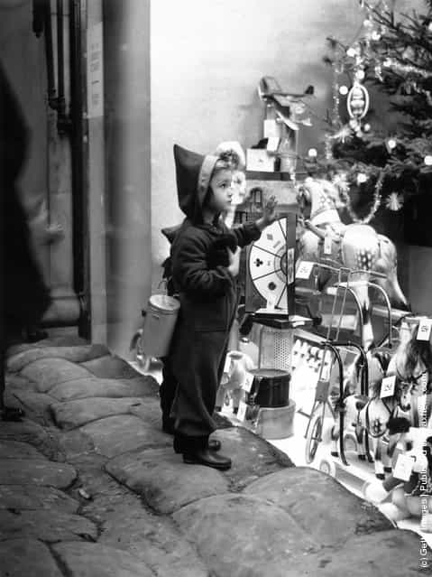1939: A seasonably attired young shopper climbs on to the sandbags to get a closer look at the toys in a shop window in the West End of London