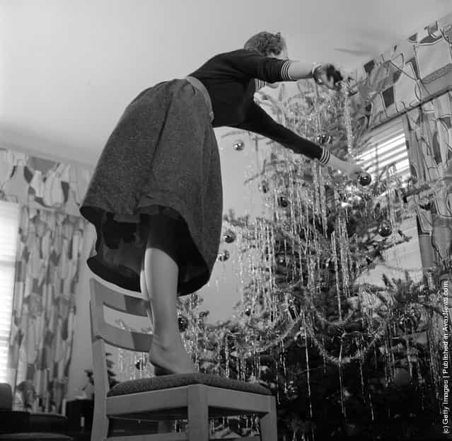 1955: When decorating a Christmas tree use a firm stepladder and dont be like this woman who is standing on a chair and leaning over too far