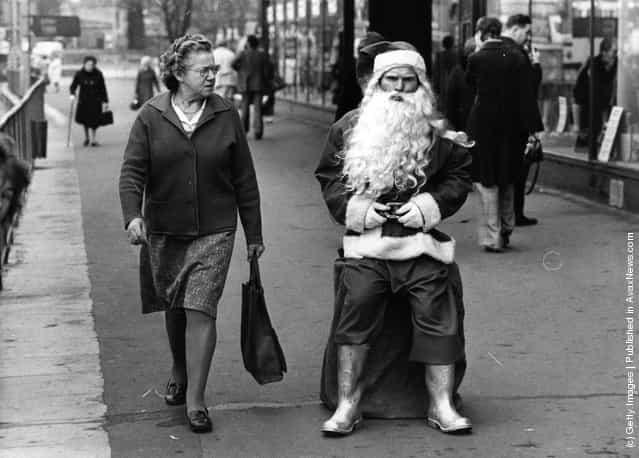 1975: A woman casts a sceptical glance at a rather surly looking man dressed as Santa in a busy shopping street