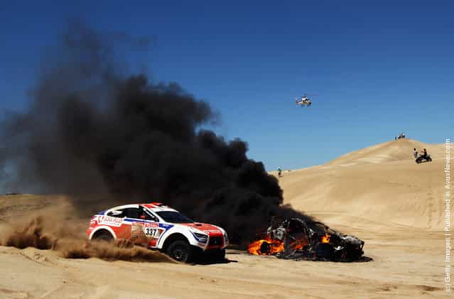 The burning car of Alfie Cox of South Africa and co-driver Jurgen Schroder sits in the sand dunes during stage one of the 2012 Dakar Rally