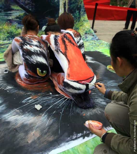 A street painter paints a tiger on the backs of three models at the Three Lanes and Seven Alleys in Fuzhou, China