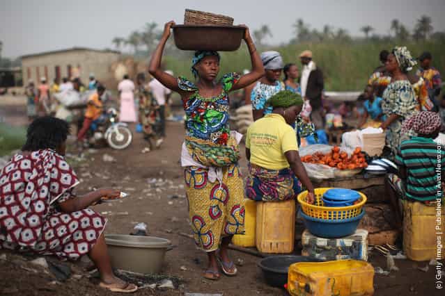 A woman carries goods while unloading her boat of produce at a market in Ganvie, near Cotonou, Benin