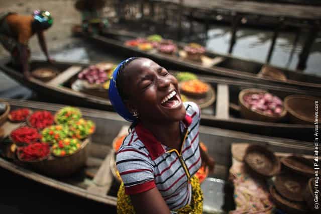 A girl laughs while unloading her boat of produce at a market in Ganvie, near Cotonou, Benin