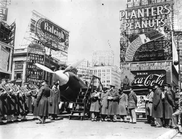 1941: A military band and a Curtiss P-40 Army Pursuit plane in Duffy Square on the corner of Times Square in New York. The plane is part of an exhibition to encourage men to join the Army Air Corps