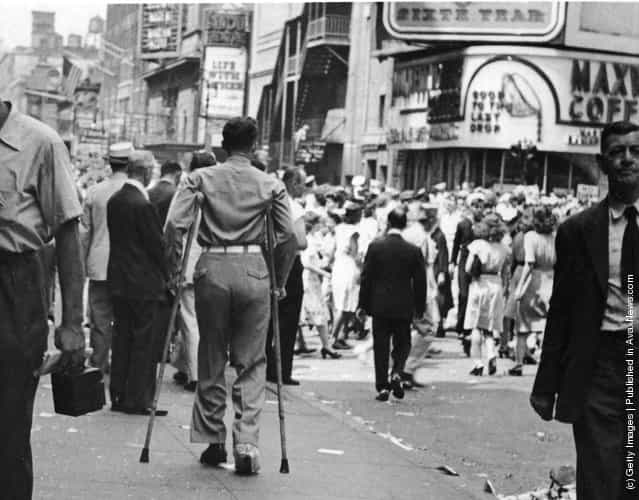 A rear veiw of a soldier on crutches in a crowd in Times Square on VJ Day, New York City, August 1945