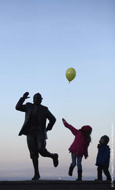 Children with balloons play beside the statue of British comedy legend Eric Morecambe